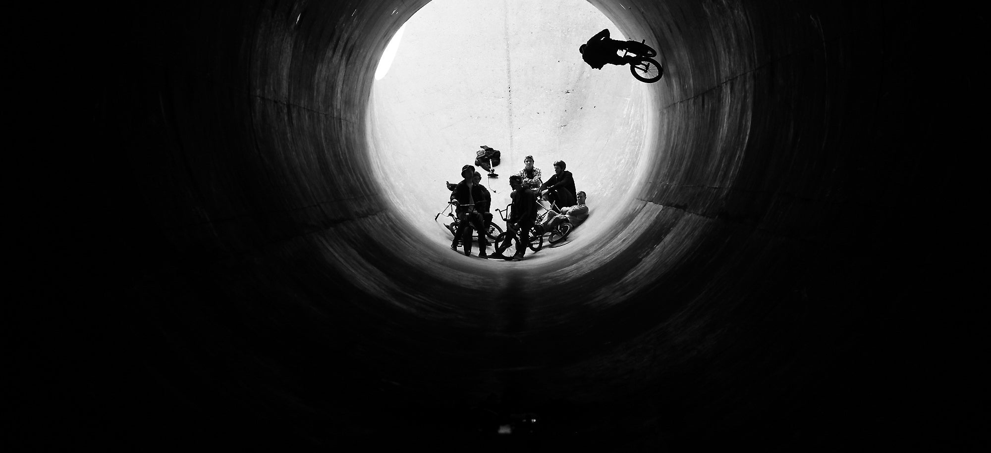 People riding BMX bicycles in a cement tube